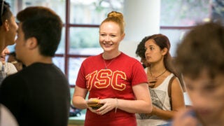 Student wearing USC branded merchandise stands in line talking with fellow students.