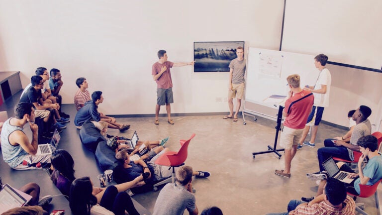 Four students giving a presentation to their class in a greek theater styled room.