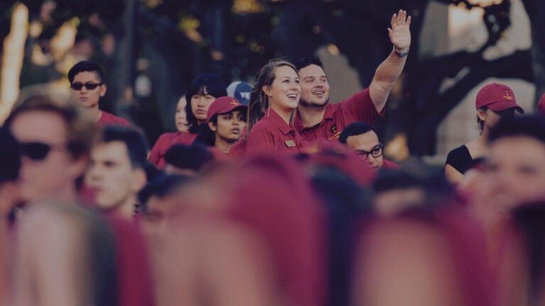 Two happy students waving amongst a crowd of students.