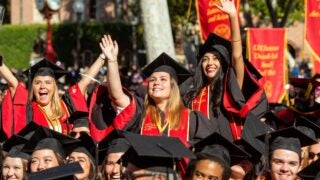 Three students students graduating from the Keck School of Medicine cheer proudly wearing their graduation cap and gown at Commencement.