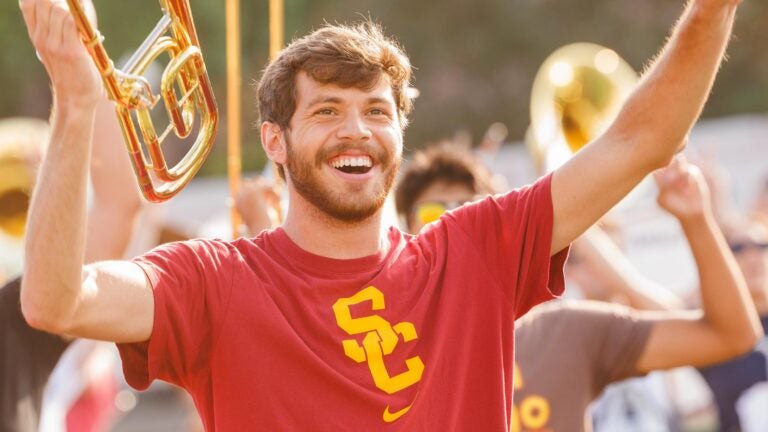 Student wearing USC branded t-shirt cheers while holding up instrument.