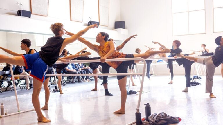 Students in a dance class hold the ballet pose, arabesque, while holding onto the bars.