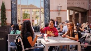 Three students sitting outside the Ronald Tutor Center eating lunch on a bright Los Angeles Day.