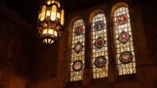 Three stained glass windows in the entrance of the Doheny Memorial Library and a large chandelier with similar art depictions as stained glass hanging down.