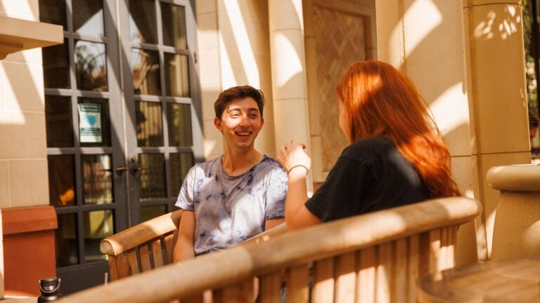 Two students talking on a bench at the School of Cinematic Arts courtyard.