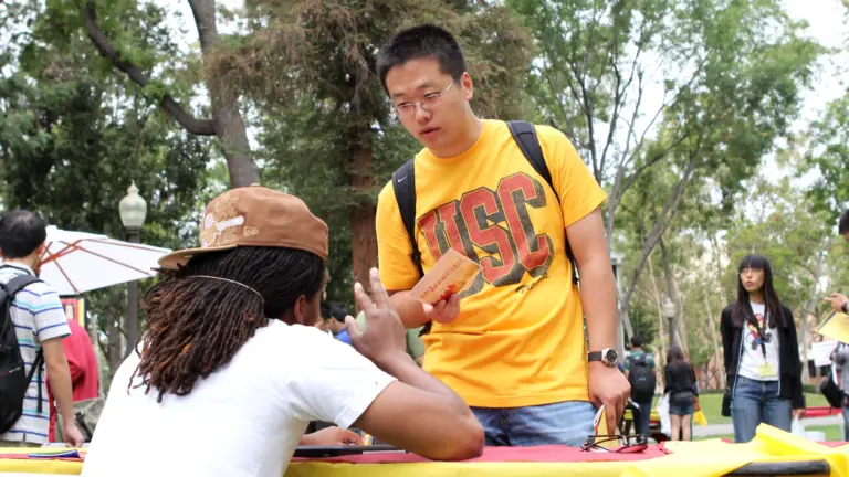Student wearing yellow USC branded shirt checks into an Orientation event at the front desk.