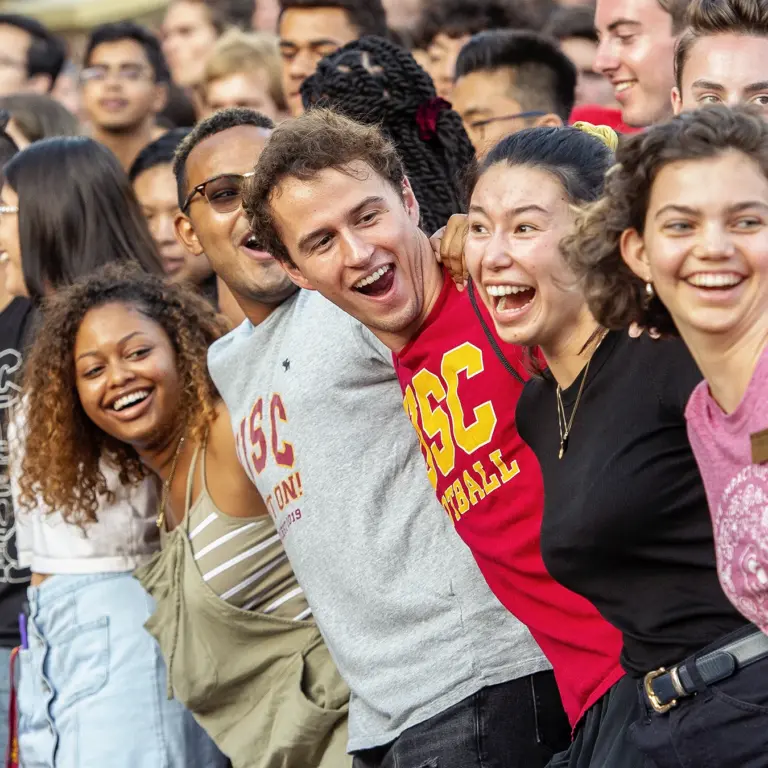 Students link arms and cheerfully laugh at a USC event.